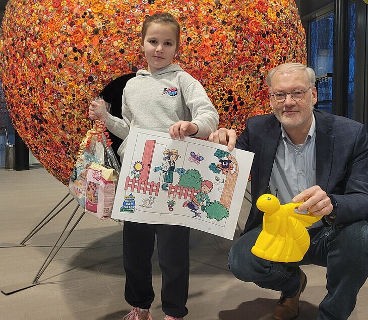 wethouder en winnares met de kleurplaat poserend voor de bol in het gemeentehuis