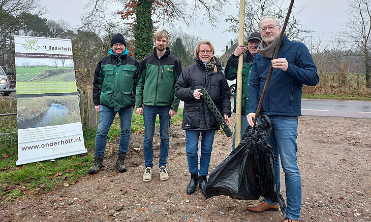 foto van de wethouder die een boom vasthoudt en een aantal vrijwilligers bij een informatiebord